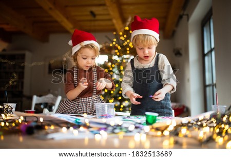Portrait of small girl and boy indoors at home at Christmas, doing art and craft.