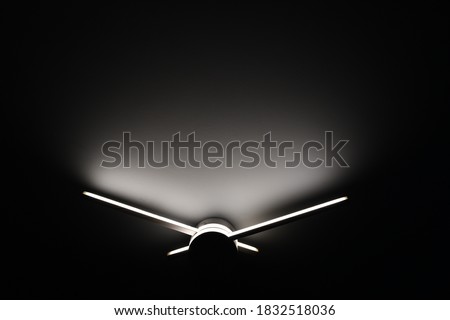 Abstract sconce lamp in shape of clock hands. Led lighting lamp closeup in darkness. Light and shadow abstraction  Royalty-Free Stock Photo #1832518036