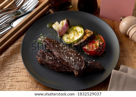 Roasted beef fillet, dark and yummy, with grilled vegetables as a side dish, knife, fork and pepper shaker aside on a wooden table