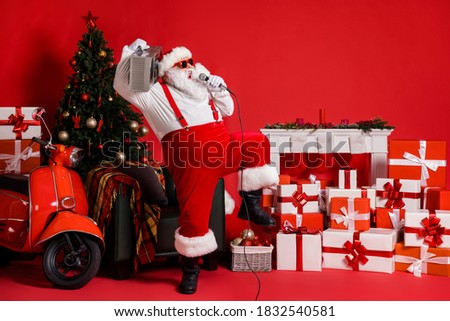 Full length photo of crazy santa claus in costume hold boom box sing mic song isolated on red color background with x-mas christmas tree