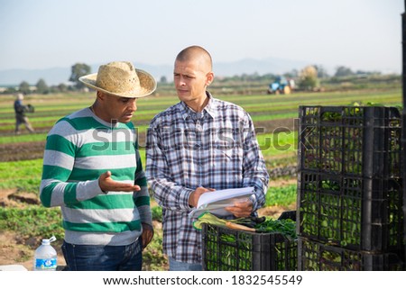 Two males farm workers talking and signing documents outdoors