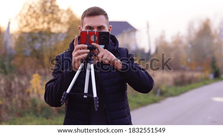 a young man of European appearance in a medical mask takes pictures of autumn nature on a phone with a tripod