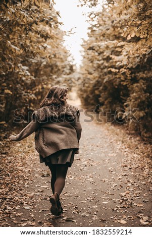 Portrait of a beautiful young happy blonde woman in a knitted sweater and dress walks, running in the park with yellow fallen autumn leaves. Warm colors, yellow and brown. October, inspiration, trees.