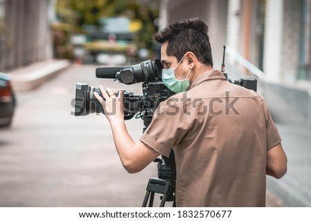Young cameraman using a professional camcorder outdoor filming news while wearing mask prevent Covid-19 or coronavirus quarantine pandemic. Royalty-Free Stock Photo #1832570677