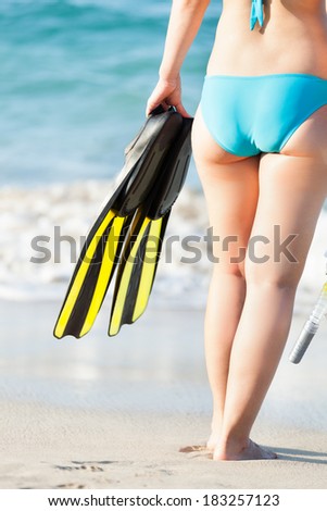 Full length rear view of woman in bikini holding diving equipment at seashore