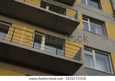 Photo of part of the building's facade. Balconies, metal railings, and Windows form linear patterns. The style of constructivism. Yellow spots on a gray background.