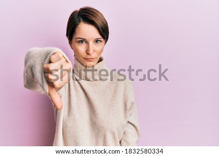 Young brunette woman with short hair wearing casual winter sweater looking unhappy and angry showing rejection and negative with thumbs down gesture. bad expression. 