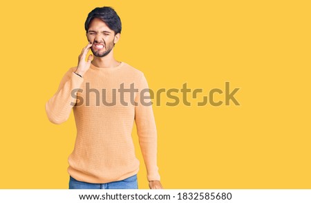 Handsome hispanic man wearing casual sweater touching mouth with hand with painful expression because of toothache or dental illness on teeth. dentist 