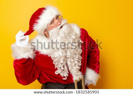 Santa Claus holding his hat, having fun during winter holiday season isolated on yellow colored background