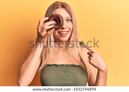 Young blonde woman holding donut smiling happy pointing with hand and finger 