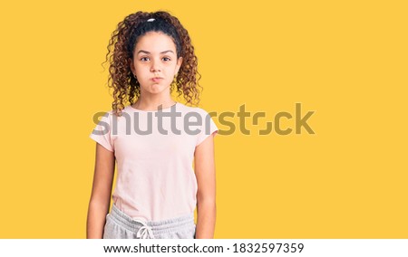 Beautiful kid girl with curly hair wearing casual clothes puffing cheeks with funny face. mouth inflated with air, crazy expression. 