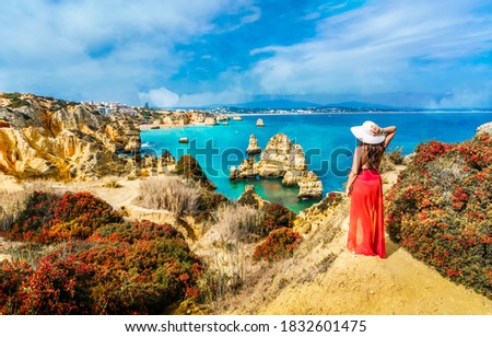 Landscape with unknown tourist girl is looking to the amazing view of spectacular rock formations, with caves, grottoes and sea arches in Lagos, Algarve, Portugal Royalty-Free Stock Photo #1832601475