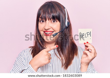 Young plus size woman wearing call center agent headset holding help reminder smiling happy pointing with hand and finger 