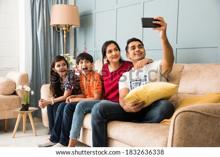 Indian family sitting on sofa and taking selfie picture using smartphone