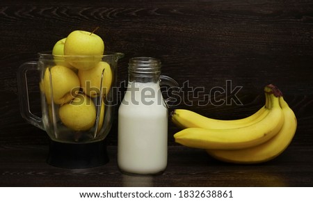 full blender with yellow apples near standing milk bottle and fresh bananas. ingredients for smoothie
