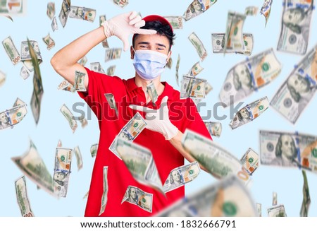 Young hispanic man wearing delivery uniform and medical mask smiling making frame with hands and fingers with happy face. creativity and photography concept.