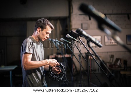 Theater audio technician adjusting an microphones on the scene. Installing and testing the sound system in the background