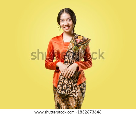Beautiful young indonesian woman wearing modern kebaya kutu baru with batik shawl isolated on yellow background Royalty-Free Stock Photo #1832673646