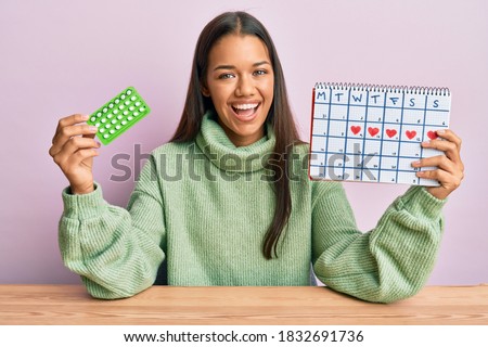Beautiful hispanic woman holding birth control pills smiling and laughing hard out loud because funny crazy joke. 