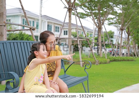 Asian child girl point to looking something with mother in summer park. Mum and daughter relaxing sitting on bench in garden outdoors