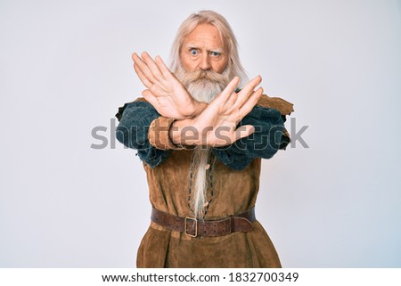Old senior man with grey hair and long beard wearing viking traditional costume rejection expression crossing arms doing negative sign, angry face 