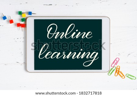 Online learning - handwritten inscription on a tablet. The concept of distance training for children. Tablet and office supplies on a white wooden background.