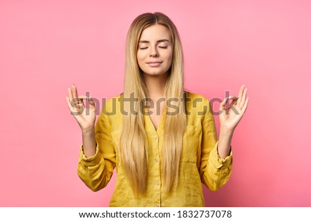 Blond beautiful young woman makes a sign of mudra, relaxes after a hard day at work, keeps her eyes closed, does yoga on a pink background. Young beautiful woman meditates indoors. Relaxation concept