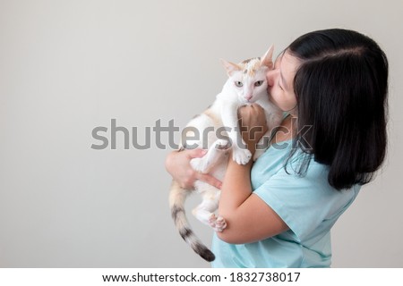 An Asian woman lovingly holds a cat and kisses it. This picture has space for putting description.