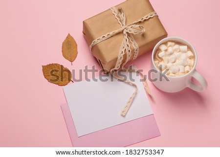 Close up of hot chocolate with marshmallows, white card blank and gift, autumn concept. Copy space, top view, flat lay