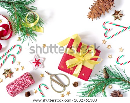 Christmas composition, greeting card. The gift wrapped in red wrapping paper is tied with a yellow ribbon with a bow. The layout is decorated with green pine branches with cones and golden stars.