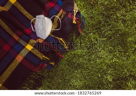 Black picnic blanket stretched out on a thick green grass blanket in the Juan Carlos I public park in Madrid on which there is a mask to prevent the spread of the coronavirus