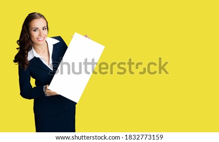 Happy smiling woman in black confident suit and white blouse showing blank signboard. Business and advertising concept. Copy space empty place for some text. Yellow color background. Advertisiment ad	