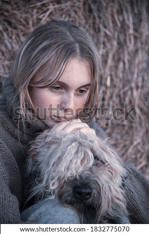 Portrait of a girl and a dog, an Irish wheat soft-coated Terrier, on the background of a haystack.