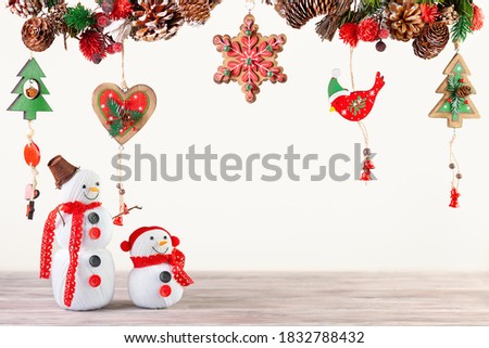 Winter festive concept with handmade snowman. Christmas or New Year decor with hanging garland of fir branches, red berries, pine cones and other wooden ornaments.
