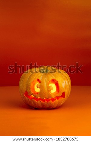 Carved and illuminated halloween pumpkin with crazy face on orange background