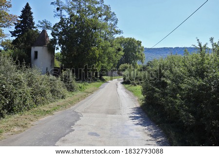 Rural country road through beautiful French countryside with an old city wall with a tower on the side.