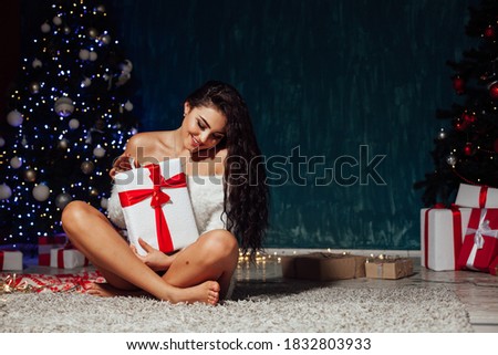Beautiful brunette woman with gifts at the Christmas tree lights garlands new year