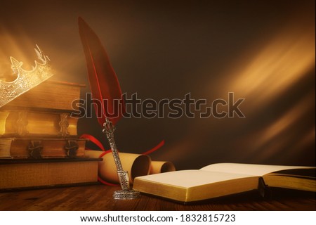 low key image of beautiful queen/king crown over old book and feather quill ink pen over wooden table. fantasy medieval period Royalty-Free Stock Photo #1832815723