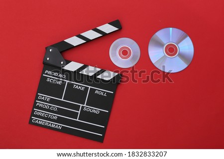 Film clapper board and cd's on red background. Cinema industry, entertainment. Top view