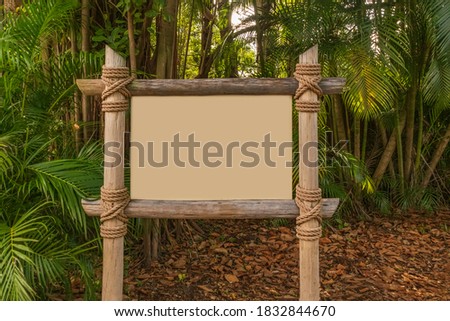 Blank signage made of natural wooden poles tied together with rope in a forest.  A blank sign ready to add your own graphic designs sits in a tropical lush forest.