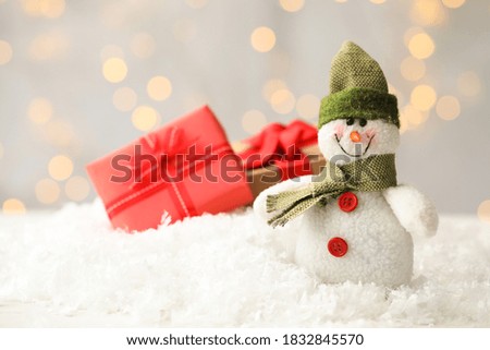 Snowman toy on snow against blurred festive lights, space for text. Christmas decoration