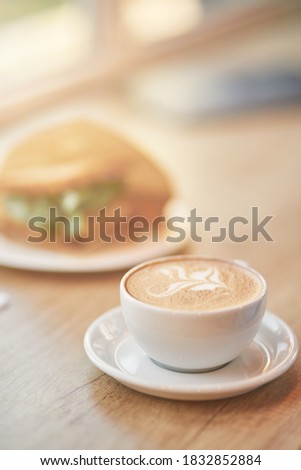 Vertical close up shot of of a cup of coffee cappuccino and sandwich on wooden table in cafe, selective focus