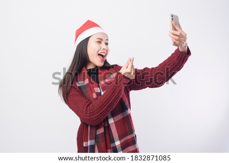 A young smiling woman wearing red Santa Claus hat taking a selfie on white background studio.