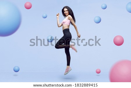 Amazing woman in trendy sportswear jumping. Smiling beautiful slim brunette young girl in fashion leggings and pink top expressing happy emotions. Blue background.