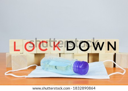 Front view of wooden block with text LOCK DOWN on white background. Wooden block with hand sanitizer and face mask. Coronavirus covid 19 concept. Selective focus.