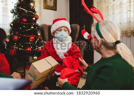 Cute boy with his grandmother wearing facemask while celebrating Christmas at home during the COVID-19 pandemic