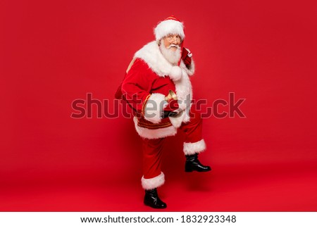 Happy, real, funny Santa Claus holding sack bag with Merry Christmas presents , delivering xmas gifts. Red background, a lot of copy space.