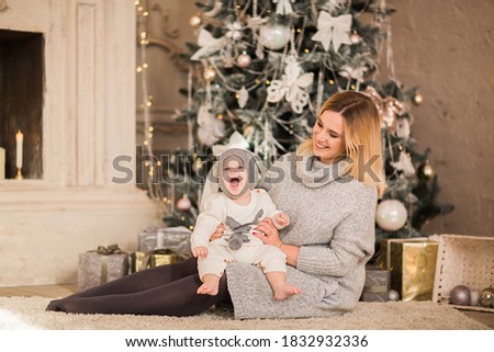 Young pretty blond haired mother posing with her little baby boy in Christmas suit like a rabbit on a white Christmas background.