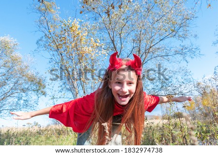 Child in a devil costume with horns. Red cloak and scary face emotion.