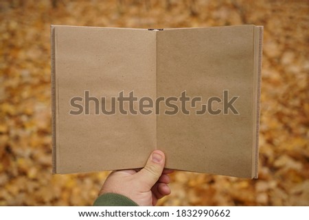 male hand holding open book on  autumn park background. Craft paper